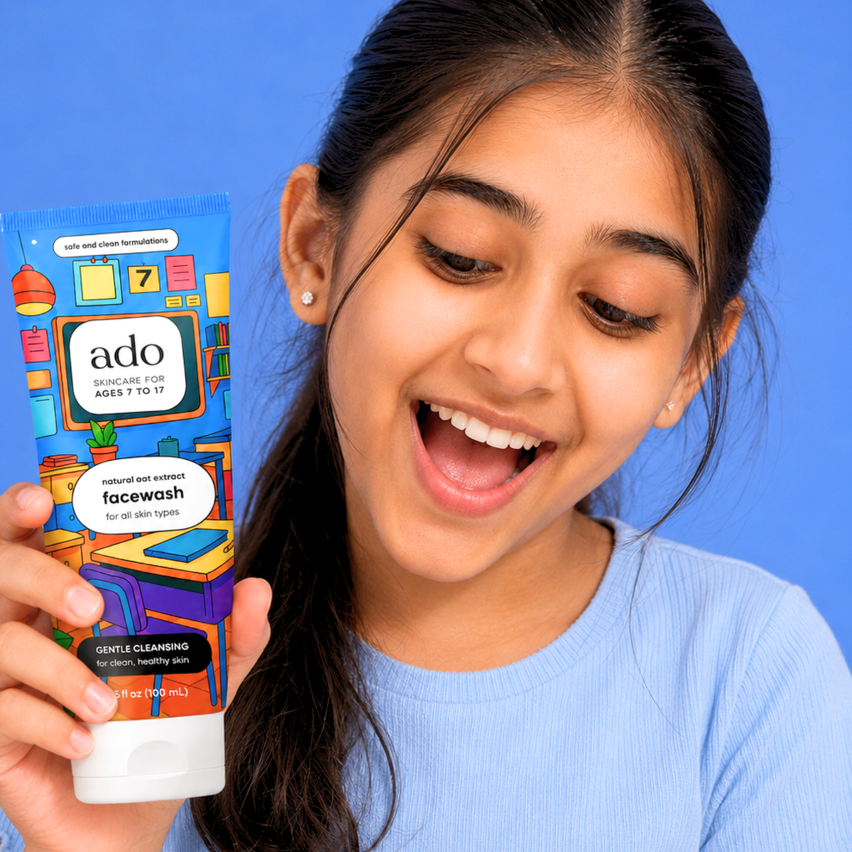 Laughing girl holding up the ado Gentle Oat Facewash tube against a blue background