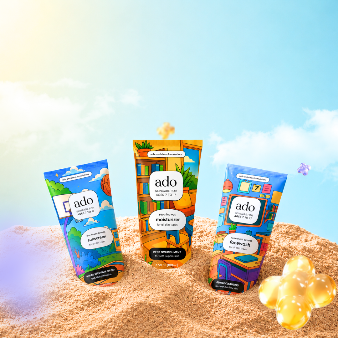 The three ado tubes, sunscreen, moisturiser and facewash, standing in warm sand under a blue sky