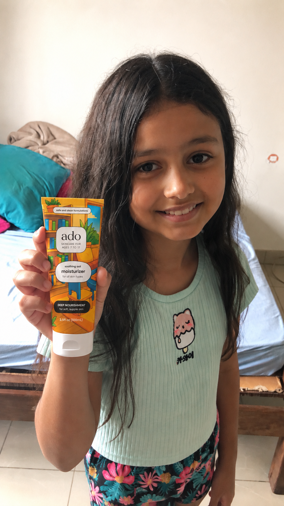 Smiling girl in a mint top holding up the ado Daily Moisturiser tube in her bedroom