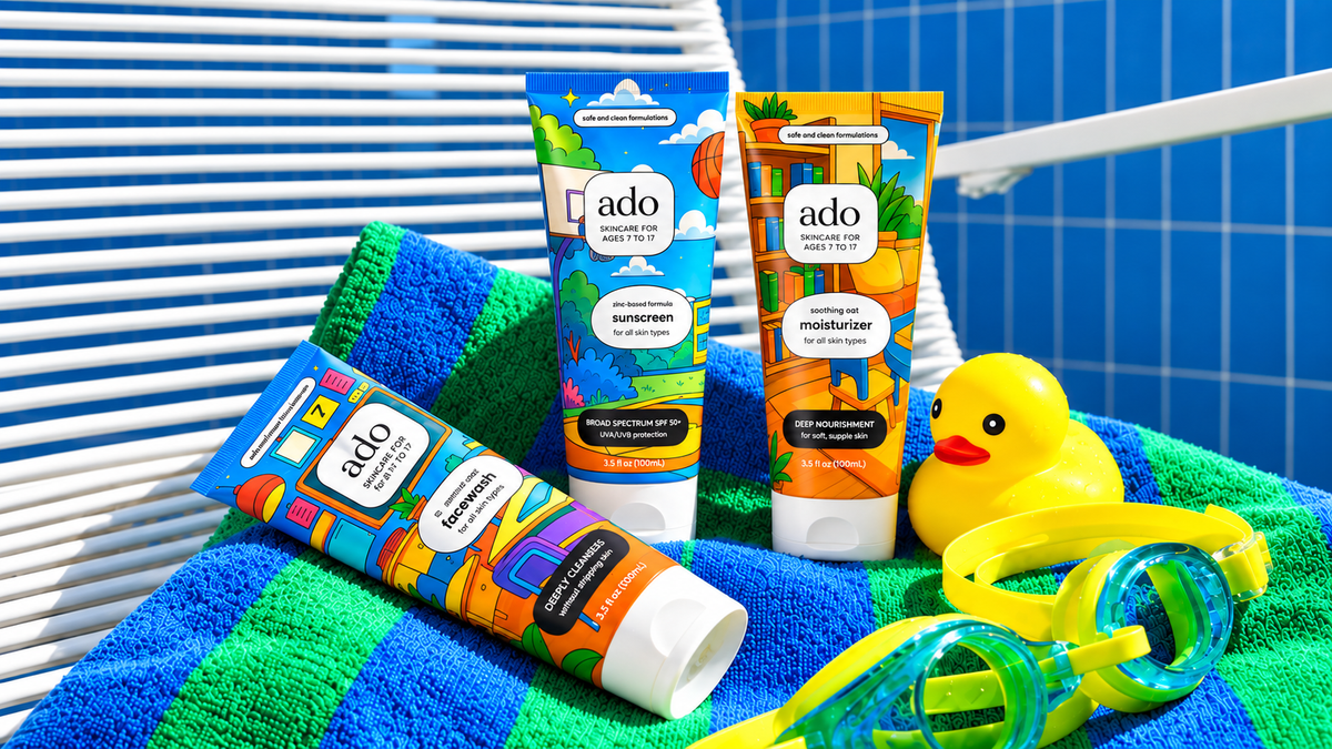 ado facewash, sunscreen and moisturiser tubes on a striped beach towel with a rubber duck and swim goggles